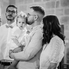 Un père embrasse sa fille, une petite fille en robe blanche, lors de son baptême. La question "jusqu'à quel âge peut-on baptiser ?" se pose.