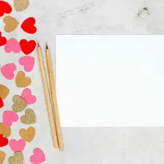 Cœurs rouges, roses et dorés pour une **journée Saint-Valentin** à écrire sur une feuille blanche avec deux crayons.