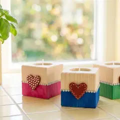 Trois bougeoirs personnalisés en bois, décorés de cœurs et de strass, sur un rebord de fenêtre.