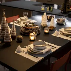 Table dressée pour le réveillon du nouvel an, avec des sapins décoratifs, des bougies et des verres.