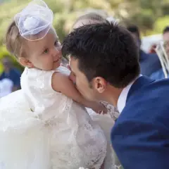 Un homme embrasse la joue d'un bébé en robe blanche, peut-être lors d'un mariage et baptême le même jour.