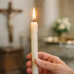 Main tenant une main pour allumer un cierge dans une église, avec une croix en arrière-plan.