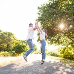 Un couple saute de joie sur un chemin ensoleillé, une belle photo d'engagement dans la nature.