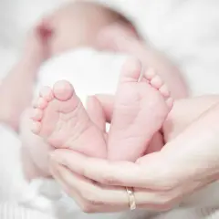 Les petits pieds d'un nourrisson de 40 jours, tendrement tenus dans des mains. Une image évoquant la douceur et la pureté, souvent associée aux traditions islamiques.
