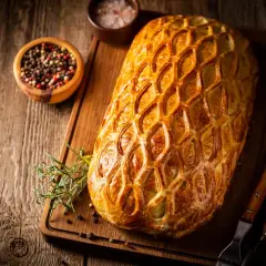 Un rôti en croûte dorée, prêt pour un menu de baptême à préparer la veille. Poivre et romarin à proximité.