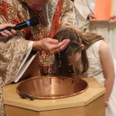 Cérémonie de baptême d'enfants : un prêtre verse de l'eau sur la tête d'une jeune fille dans une église.