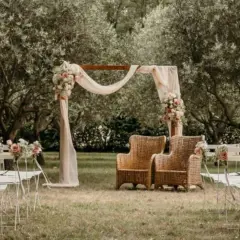 Un bel exemple de cérémonie laïque en plein air, avec un arche fleuri, des chaises blanches et deux fauteuils en rotin sous les oliviers.