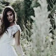 Une mariée en robe blanche, cheveux longs et ondulés, pose dans un champ fleuri. Ambiance romantique pour un mariage bohème.