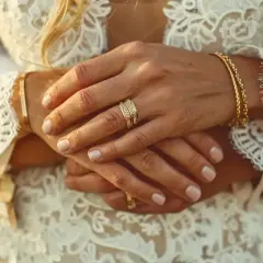 Mains jointes, alliances étincelantes sur une robe de mariée en dentelle. L'image évoque de beaux textes pour un mariage civil, symbolisant l'union et l'amour éternel.