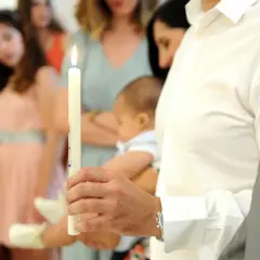 Un homme tient une bougie allumée, symbole de la lumière divine, lors d'un baptême. Il porte un bébé, prêt à accepter d'être parrain.