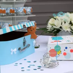 Décoration pour organiser un baptême : boîte à trésors bleue, ours en biscuit "Merci", fleurs blanches et boîtes cadeaux colorées.