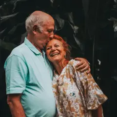 Un couple âgé s'embrasse tendrement, un moment de joie pour fêter sa retraite en famille.