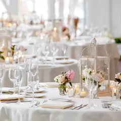 Disposition table mariage élégante avec lanternes, bougies et bouquets de roses. Vaisselle et verres prêts pour les invités.