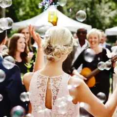 Une marraine, entourée de bulles, tient un bouquet de roses. Une femme joue de la guitare en arrière-plan.