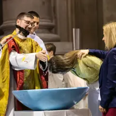 Cérémonie de baptiser en arabe. Un prêtre verse de l'eau sur la tête d'une femme dans un bassin bleu.