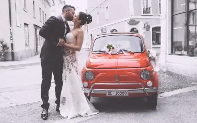 Un couple s'embrasse devant une Fiat 500 rouge décorée, un doux souvenir de leur mariage à deux à l'étranger.