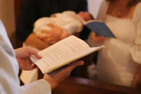 Célébration d'un baptême : un livre ouvert est tenu, un bébé est porté, et des parents écoutent attentivement la bénédiction.