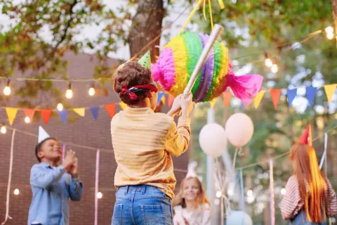 Enfants en fête, un garçon bandeau sur les yeux s'apprête à frapper une pinata colorée. L'art de fabriquer une pinata pour un joyeux anniversaire.