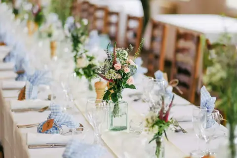 Décoration baptême champêtre à faire soi-même : table dressée avec nappes blanches, bouquets de fleurs sauvages, serviettes à carreaux bleus et bois.