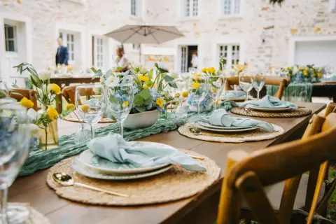 Table dressée pour un thème anniversaire adulte, avec des fleurs bleues et jaunes, des serviettes bleu pâle et des couverts dorés.
