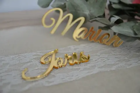 Marque place plexiglas doré "Joris" et "Marion" sur un chemin de table en dentelle, avec des feuilles d'eucalyptus en arrière-plan.
