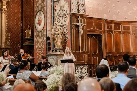 Une femme chante lors d'un mariage, accompagnée d'un orchestre. La prière universelle du mariage résonne dans l'église ornée.