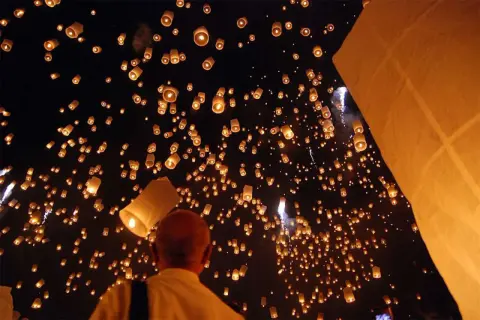 Un homme observe une multitude de lanternes thaïlandaises illuminant le ciel nocturne, créant un spectacle magique.