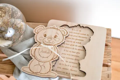 Ours en bois gravé avec le prénom Arthur, à côté d'une sphère en verre remplie de fleurs séchées.