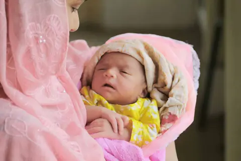 Une mère câline son nouveau-né, enveloppé dans des tissus roses et crème. Une douce image pour des douces félicitations naissance islam.