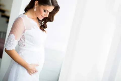 Une future mariée enceinte, vêtue d'une robe blanche, caresse son ventre avec tendresse.