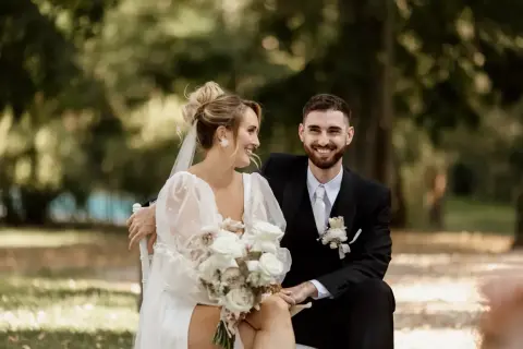 Un couple rayonnant, le marié en costume noir, la mariée en robe blanche, échangeant des regards complices lors de leur échange de voeux mariage.