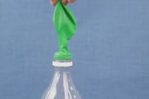Un ballon vert est posé sur le goulot d'une bouteille en plastique. Une main le tient, prêt à montrer comment gonfler un ballon.