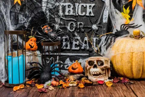 Décoration effrayante pour une **thème soirée halloween** : citrouilles, araignées, crâne, toile d'araignée et bougie bleue sur fond de pierre gravée.