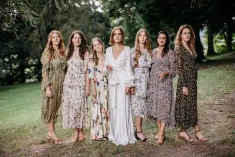 Six femmes en robes fleuries et une en blanc, probablement les témoins d'un mariage.