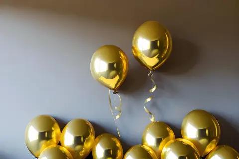 Des ballons dorés brillants flottent près d'un mur. Une astuce pour savoir comment faire tenir des ballons au plafond : utilisez du ruban adhésif double face.