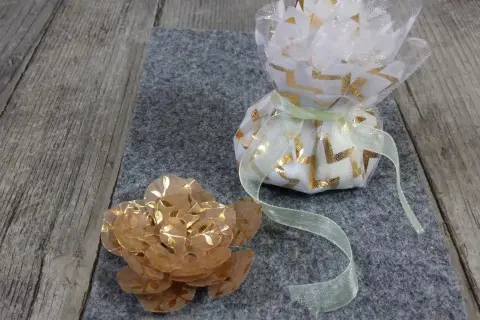 Un sachet dragees a faire soi meme, décoré de motifs dorés, à côté d'une fleur en papier.