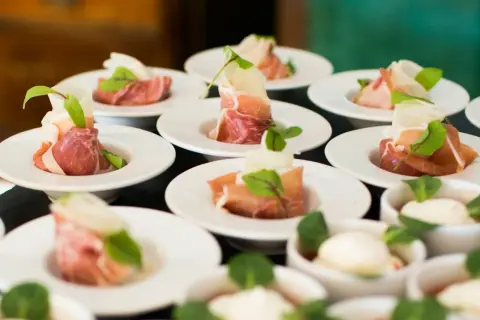 Petits amuse-bouches de jambon cru roulé, melon et garniture verte, prêts pour un dîner assis.