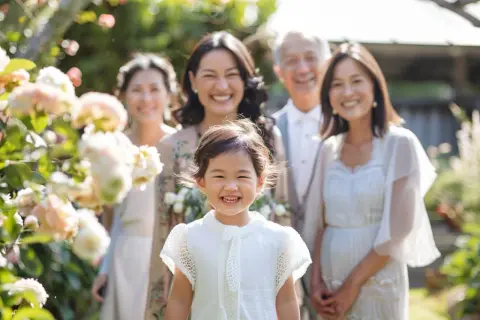Une famille souriante célèbre un baptême laïque dans un jardin fleuri. La petite fille au premier plan rayonne de joie.
