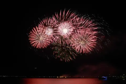 Un spectaculaire feu d'artifice illumine le ciel nocturne au-dessus de l'eau, reflétant ses couleurs vives sur la surface calme.