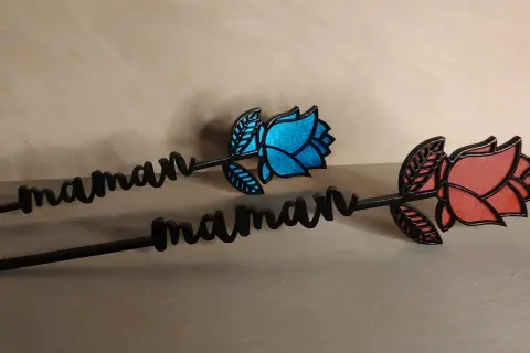 Deux roses décoratives avec le prénom "maman" gravé, l'une bleue, l'autre rouge.