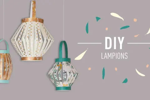 Trois lanternes en papier suspendues, décorées de motifs dorés et tropicaux.