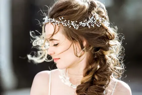Une jeune femme avec une coiffure bohème, ornée d'une tiare scintillante, ses cheveux ondulés tombant en tresse.