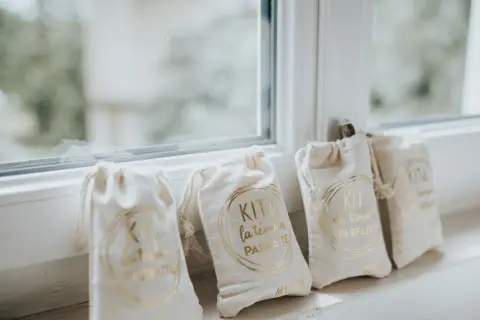 Quatre petits sacs en tissu écru, chacun portant l'inscription dorée "KIT du témoin PARFAIT". Un cadeau témoin mariage personnalisé, prêt à être offert.