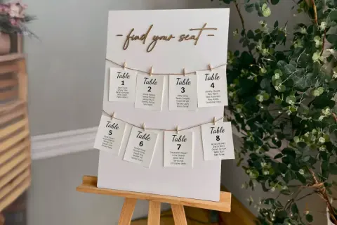 Un panneau "Trouvez votre siège" avec des cartes de table numérotées, chacune avec des noms d'invités. Un marque place vierge est visible sur la carte de la table 8.