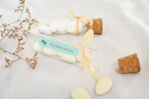 Des dragées pour créer une liste de baptême, dans des fioles décorées d'une petite voiture et du nom "Adam".