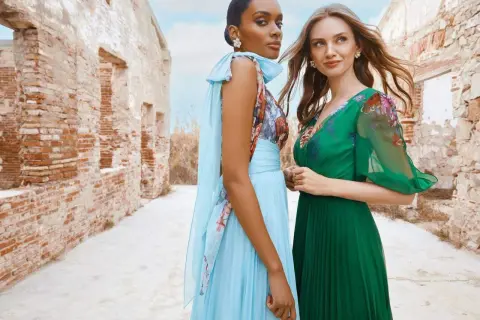 Deux femmes élégantes posent devant des ruines. L'une porte une robe bleu ciel plissée, l'autre une robe verte. Idées pour comment s'habiller pour un mariage.