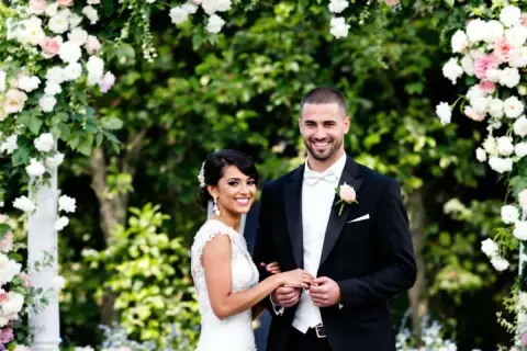 Un couple souriant, paré pour leur cérémonie d'engagement mariage, sous une arche fleurie.