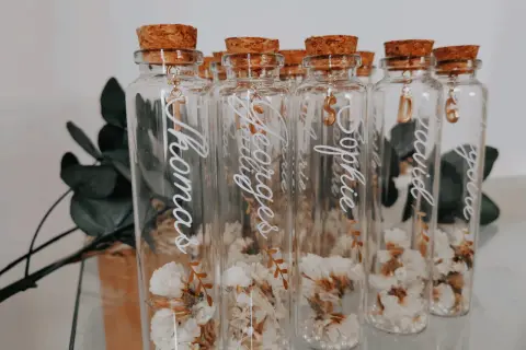Bouteilles en verre avec fleurs séchées, bouchons en liège et breloques dorées. Parfait cadeau invité bapteme diy personnalisé avec des prénoms.