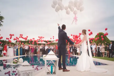 Mariés lançant des ballons rouges et blancs lors d'une animation mariage, avec des invités autour d'une piscine.