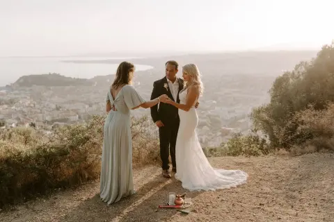 Cérémonie d'elopement mariage intime au sommet d'une colline, avec vue sur une ville et la mer. Le couple échange ses vœux, officiés par une amie.